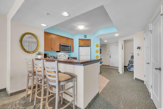 kitchen featuring white refrigerator, kitchen peninsula, carpet floors, a textured ceiling, and a breakfast bar