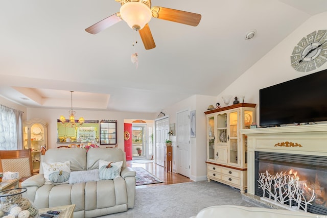 living room with ceiling fan with notable chandelier, vaulted ceiling, a raised ceiling, and light carpet