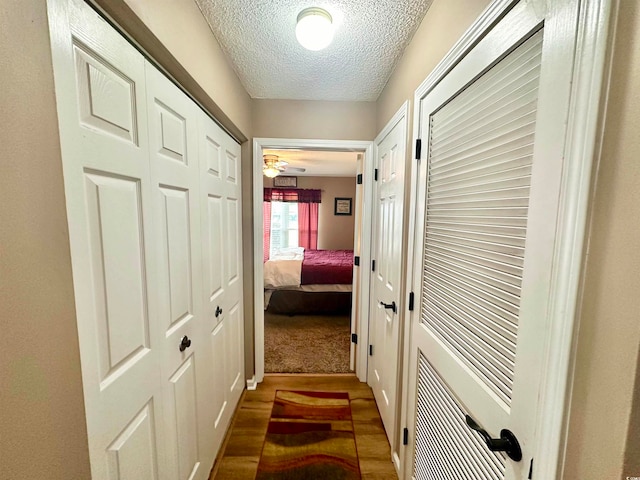 corridor featuring a textured ceiling and dark carpet