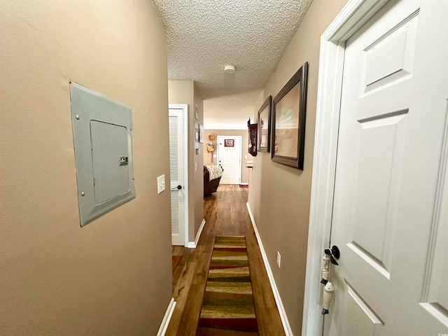 corridor with electric panel, a textured ceiling, and dark wood-type flooring