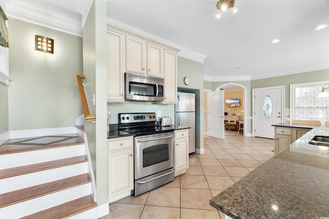 kitchen with cream cabinets, dark stone counters, light tile patterned flooring, crown molding, and appliances with stainless steel finishes