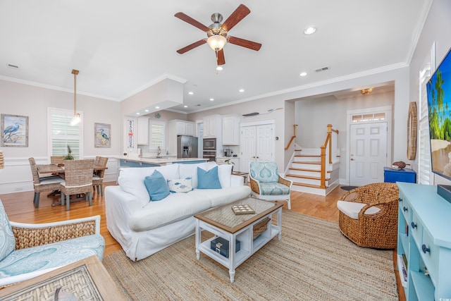 living area with a ceiling fan, crown molding, light wood-style flooring, recessed lighting, and stairway