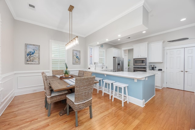 dining area with ornamental molding, light wood-style flooring, recessed lighting, and a wainscoted wall