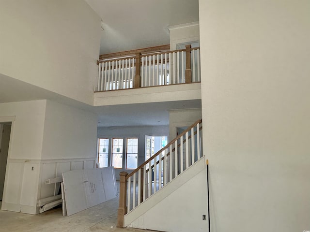 stairs featuring a towering ceiling, a decorative wall, and wainscoting