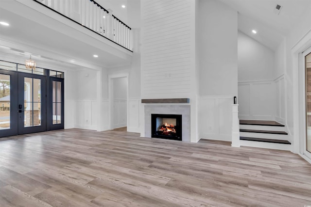 unfurnished living room with a decorative wall, a fireplace, light wood-style floors, french doors, and stairway