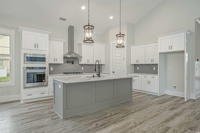 kitchen with wall chimney exhaust hood, a center island with sink, appliances with stainless steel finishes, and white cabinets