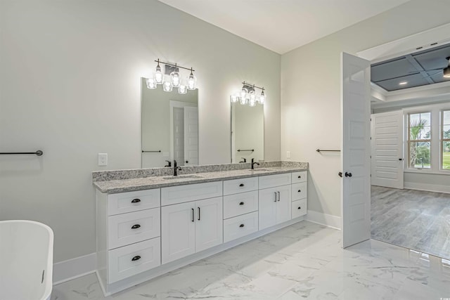 bathroom featuring double vanity, baseboards, marble finish floor, a freestanding tub, and a sink