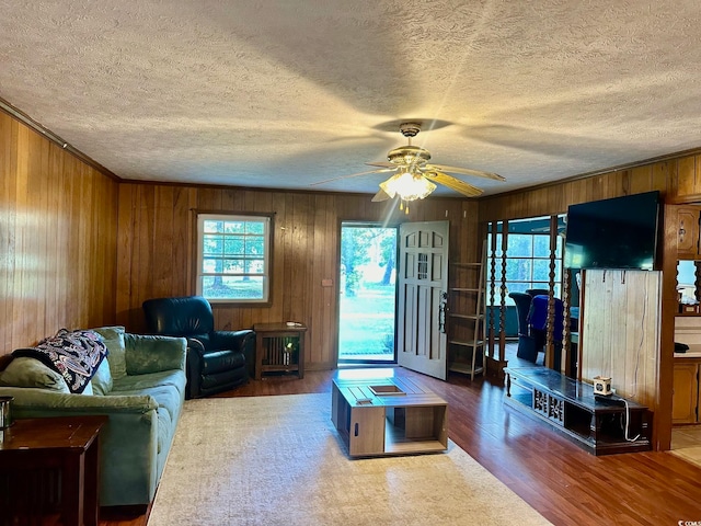 living room with wood walls, hardwood / wood-style floors, ceiling fan, and a textured ceiling