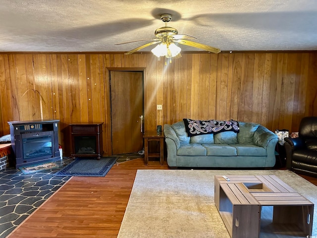 living room featuring a textured ceiling, wood-type flooring, wooden walls, and ceiling fan