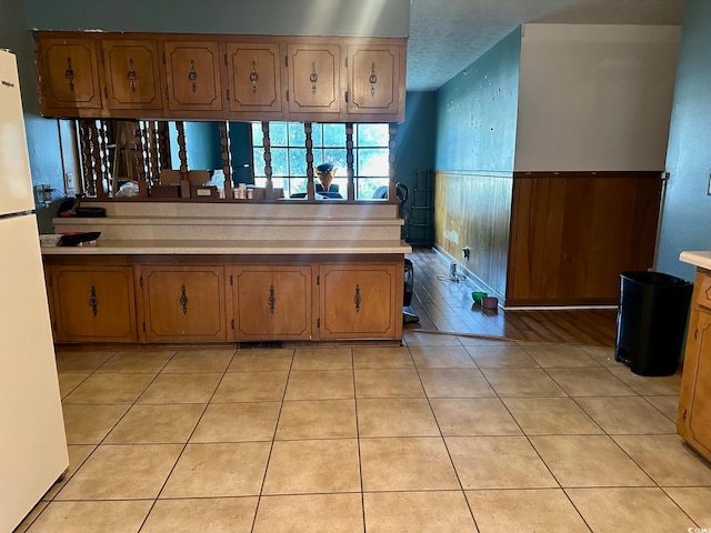 kitchen featuring wooden walls, a textured ceiling, white refrigerator, and light tile patterned floors