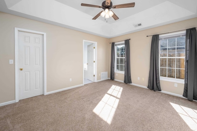 unfurnished room with a raised ceiling, ceiling fan, and light colored carpet