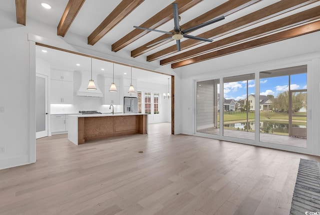 unfurnished living room with a water view, sink, ceiling fan, light hardwood / wood-style floors, and beam ceiling