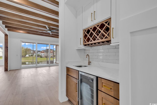 bar with light hardwood / wood-style flooring, decorative backsplash, beamed ceiling, white cabinetry, and beverage cooler