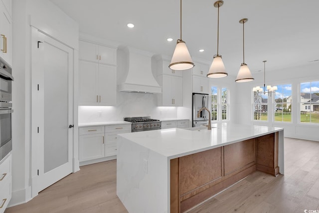 kitchen with pendant lighting, custom range hood, an island with sink, appliances with stainless steel finishes, and white cabinetry