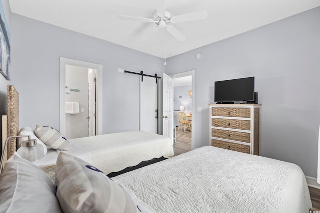 bedroom with wood-type flooring, a barn door, ceiling fan, and connected bathroom