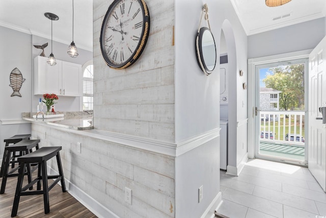 kitchen featuring white cabinets, stacked washer / dryer, kitchen peninsula, and crown molding