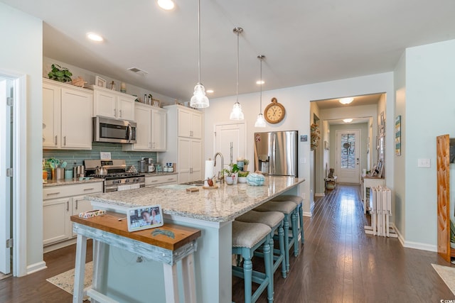 kitchen featuring white cabinets, stainless steel appliances, a kitchen island with sink, and a breakfast bar area