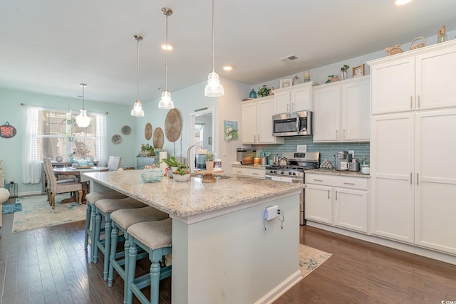 kitchen featuring an island with sink, a sink, light stone counters, dark wood finished floors, and appliances with stainless steel finishes