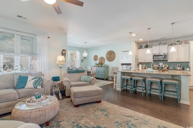 living area featuring baseboards, visible vents, dark wood-style flooring, and ceiling fan