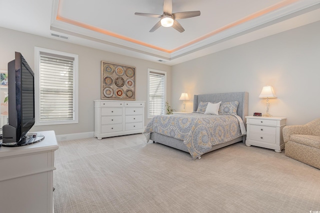 bedroom with light carpet, ceiling fan, and a tray ceiling