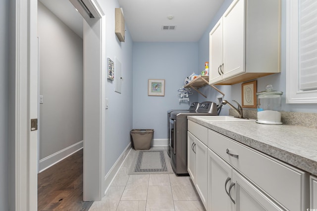 clothes washing area featuring cabinets, sink, washer and dryer, and light hardwood / wood-style flooring