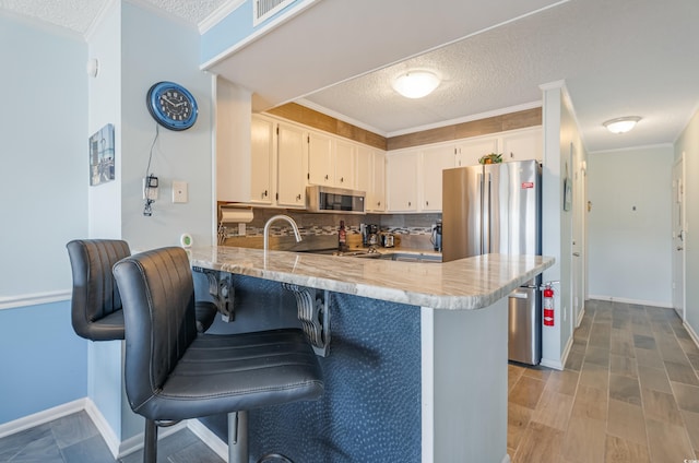 kitchen with crown molding, white cabinetry, stainless steel appliances, and kitchen peninsula