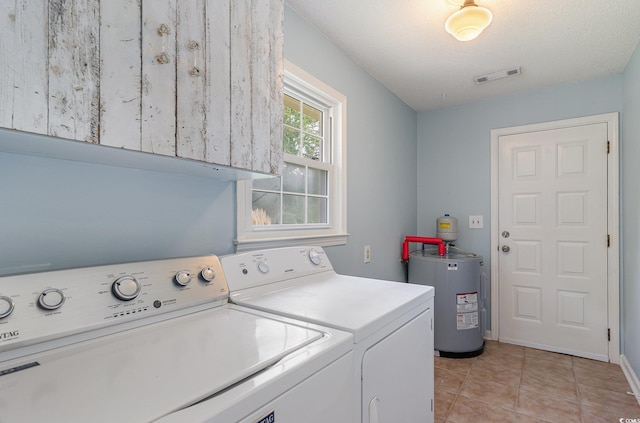 washroom with cabinets, water heater, a textured ceiling, light tile patterned floors, and washing machine and clothes dryer