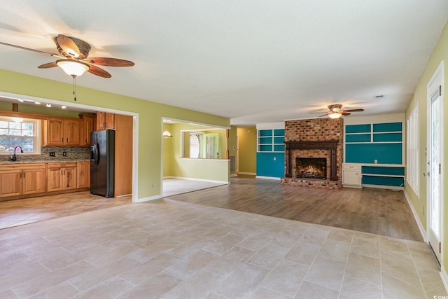 unfurnished living room featuring a fireplace, sink, light wood-type flooring, and ceiling fan