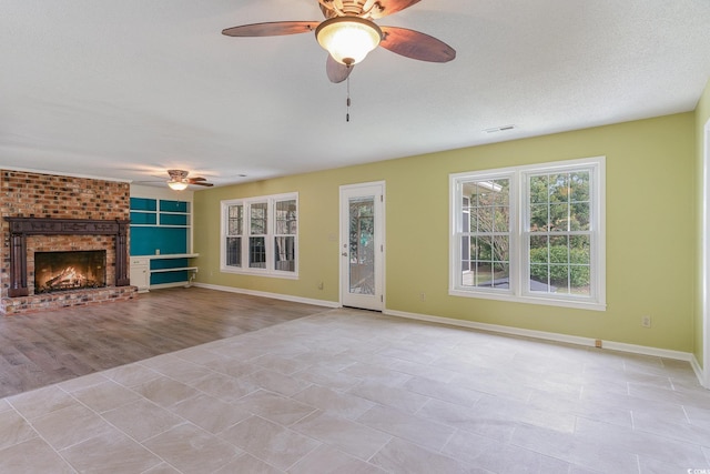 unfurnished living room with a textured ceiling, ceiling fan, a fireplace, light hardwood / wood-style flooring, and built in features