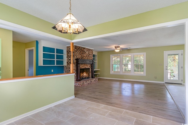 unfurnished living room with a fireplace, ceiling fan, a textured ceiling, and light wood-type flooring