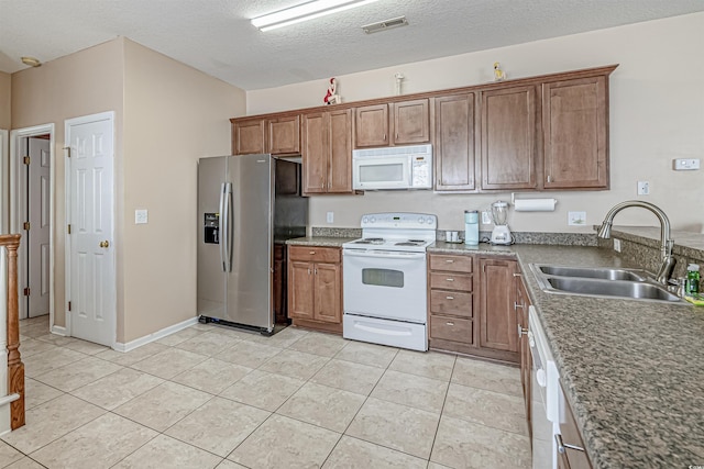 kitchen with light tile patterned flooring, white appliances, sink, and a textured ceiling