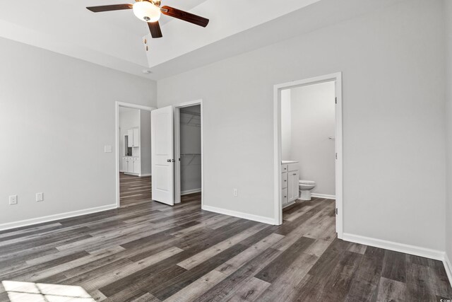 unfurnished bedroom featuring ensuite bathroom, a walk in closet, dark hardwood / wood-style flooring, a closet, and ceiling fan