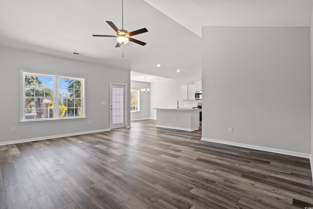 unfurnished living room featuring dark hardwood / wood-style floors, ceiling fan with notable chandelier, and high vaulted ceiling