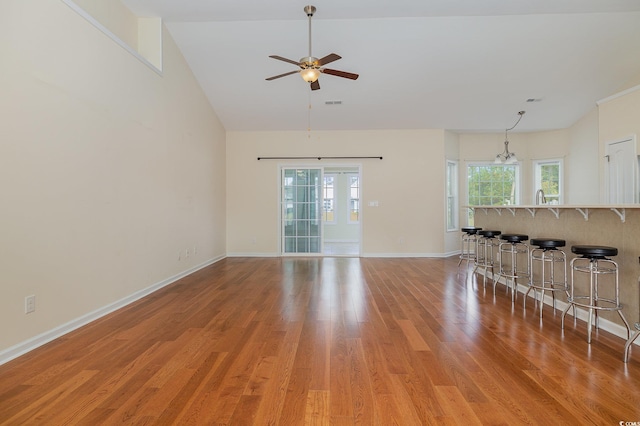 unfurnished living room with ceiling fan with notable chandelier, high vaulted ceiling, and light hardwood / wood-style floors