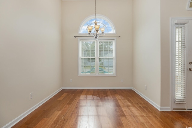 empty room featuring wood-type flooring, a towering ceiling, and a notable chandelier