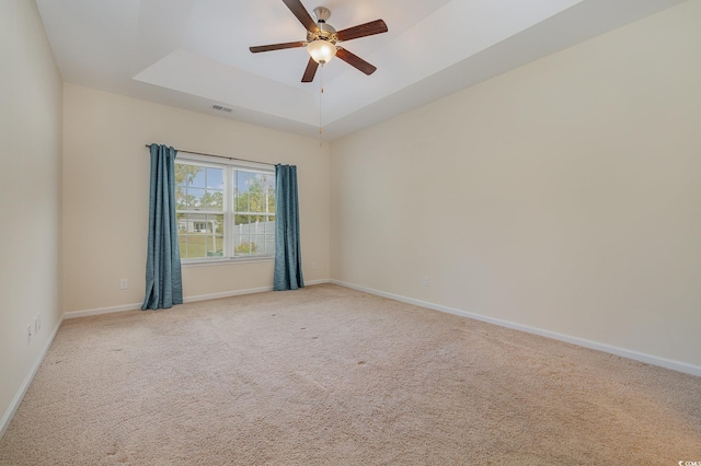 spare room featuring ceiling fan, a tray ceiling, and light colored carpet