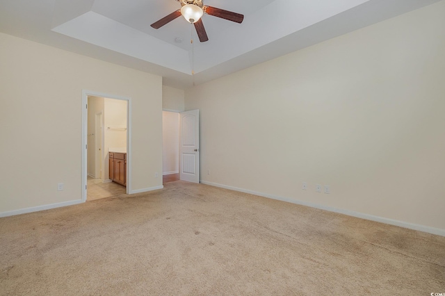 unfurnished bedroom featuring light carpet, ensuite bathroom, ceiling fan, and a tray ceiling