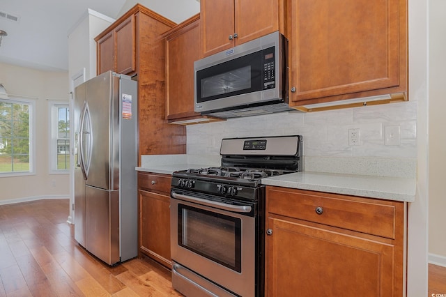 kitchen featuring light wood-type flooring, stainless steel appliances, light stone counters, and tasteful backsplash