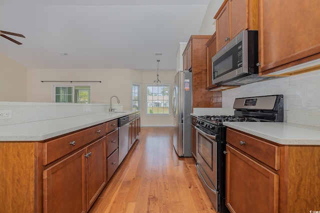 kitchen with decorative backsplash, appliances with stainless steel finishes, light stone counters, light hardwood / wood-style flooring, and hanging light fixtures