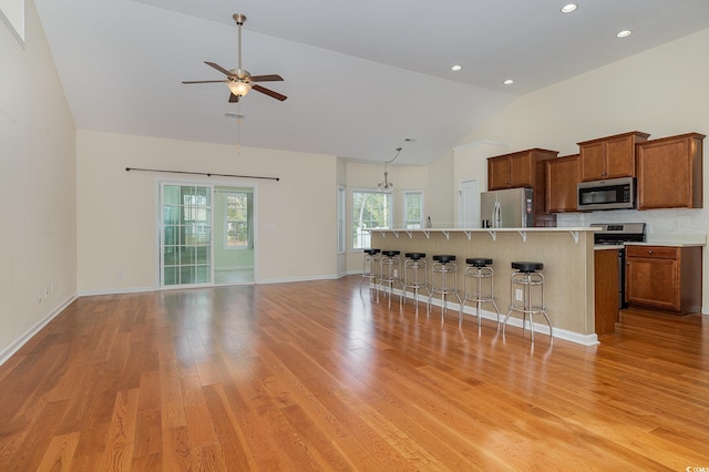 kitchen with stainless steel appliances, a kitchen breakfast bar, high vaulted ceiling, a kitchen island with sink, and light wood-type flooring