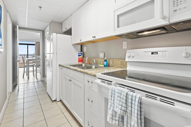 kitchen featuring sink, white appliances, white cabinets, light tile patterned flooring, and a drop ceiling