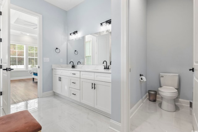 full bath with baseboards, double vanity, a sink, toilet, and connected bathroom