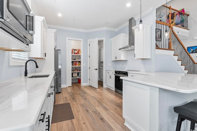 kitchen featuring light wood-type flooring, a sink, a peninsula, appliances with stainless steel finishes, and wall chimney exhaust hood