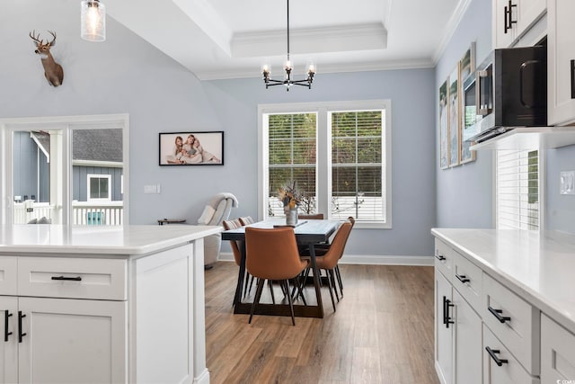 dining space with baseboards, light wood finished floors, a tray ceiling, ornamental molding, and a notable chandelier