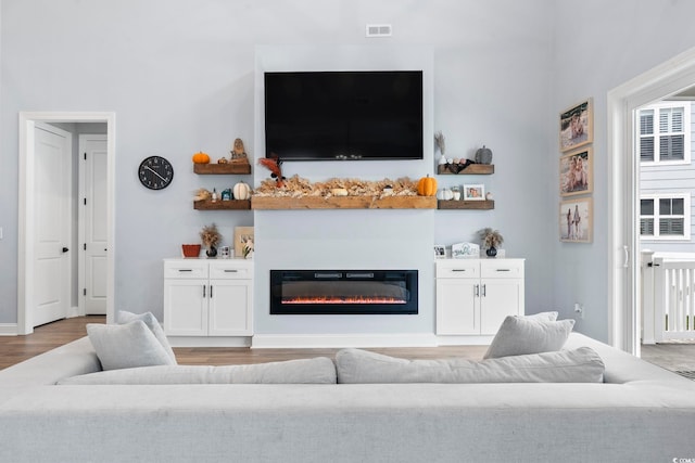 living area with visible vents, a glass covered fireplace, and light wood-style flooring