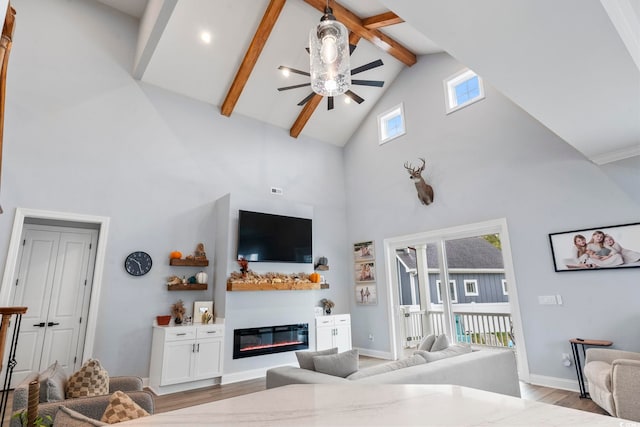 living room featuring wood finished floors, baseboards, beam ceiling, ceiling fan, and a glass covered fireplace