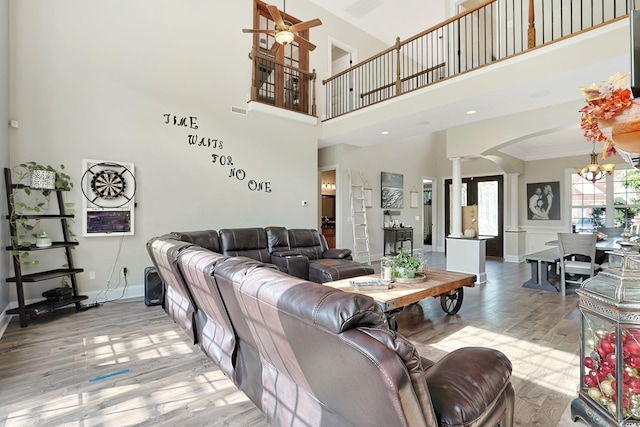 living room with crown molding, a towering ceiling, ornate columns, hardwood / wood-style flooring, and ceiling fan