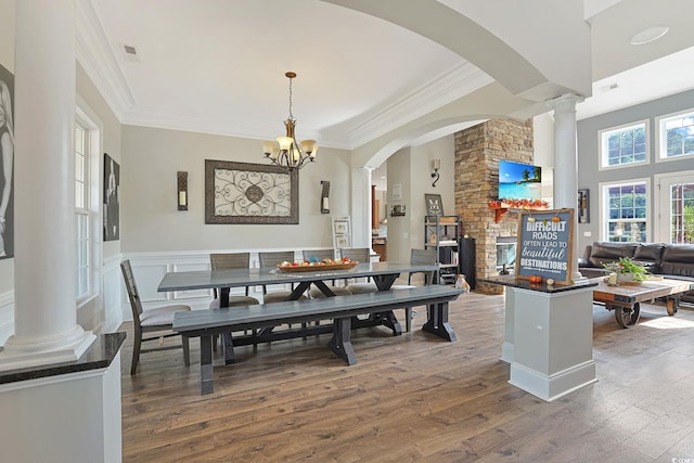 dining room featuring a stone fireplace, dark hardwood / wood-style flooring, a chandelier, and crown molding