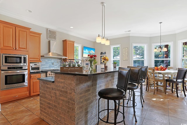 kitchen featuring a wealth of natural light, a kitchen island with sink, wall chimney exhaust hood, and stainless steel appliances