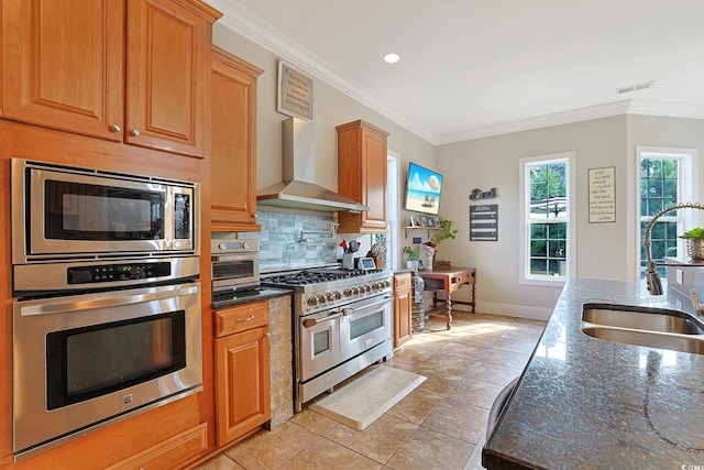 kitchen with sink, appliances with stainless steel finishes, wall chimney exhaust hood, dark stone countertops, and light tile patterned floors